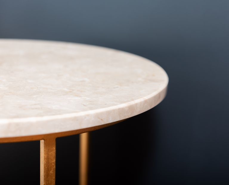 Fragment of empty marble side table on golden stand placed on blurred black background in studio