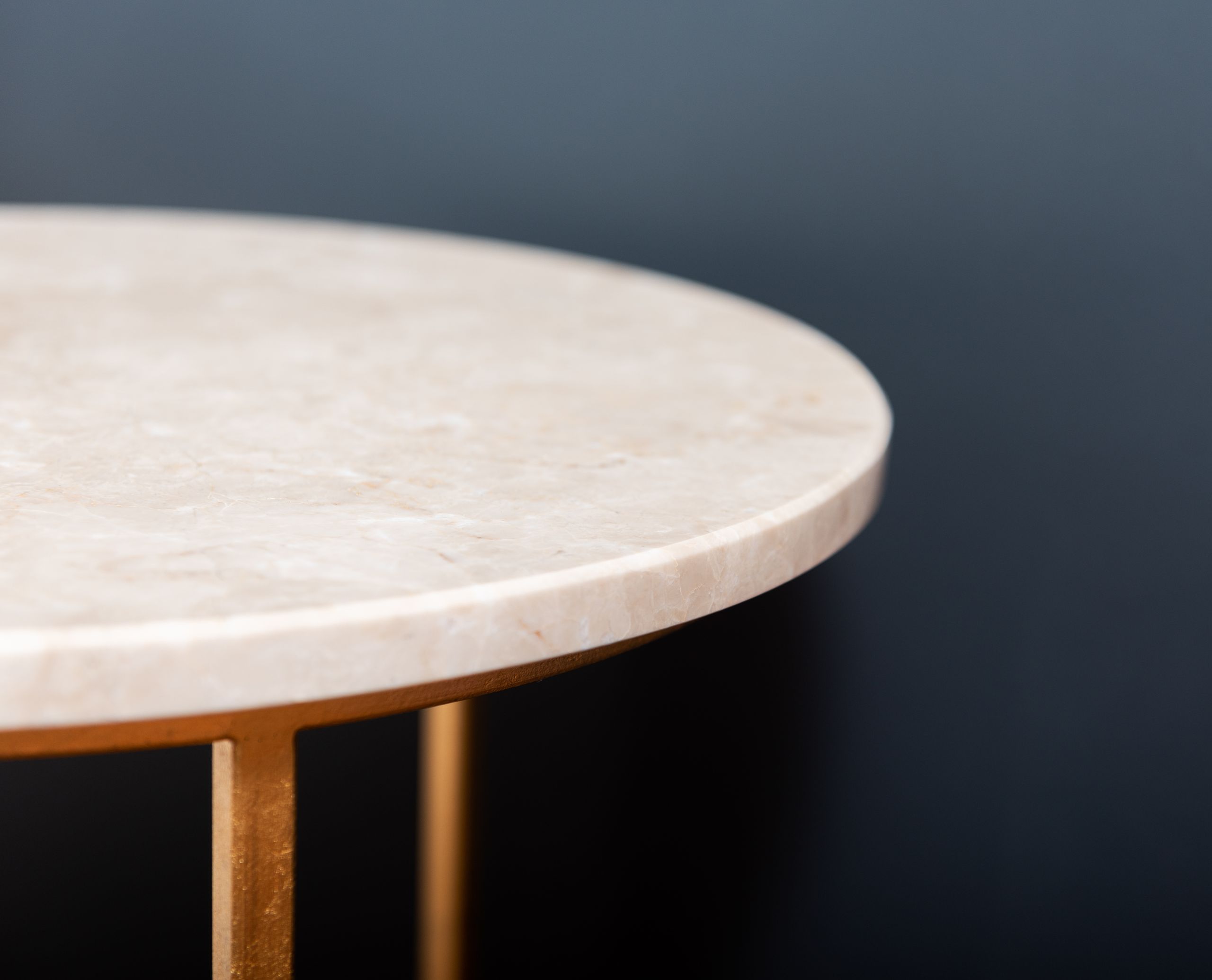 Fragment of empty marble side table on golden stand placed on blurred black background in studio